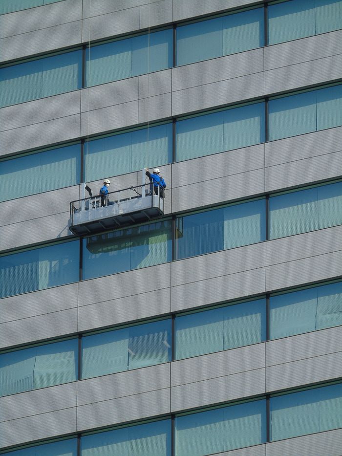 Two workers wash windows on a contemporary glass building exterior from a hanging platform.